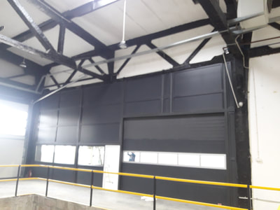 Perete despărțitor din PVC pe schelet metalic și ușă sectională cu panou vitrat culoare gri antracit in hala industrială.